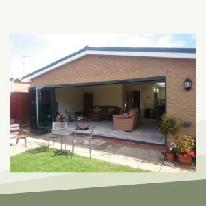 The outside of the extension with the large glass folding doors open, opening up the living room to include the sunny garden.